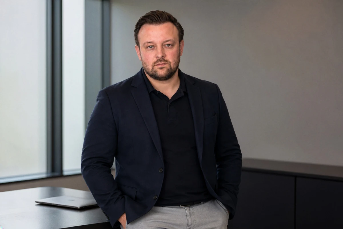 David Keiser lehnt im dunkelblauen Sakko an einem Schreibtisch im hellen Büro